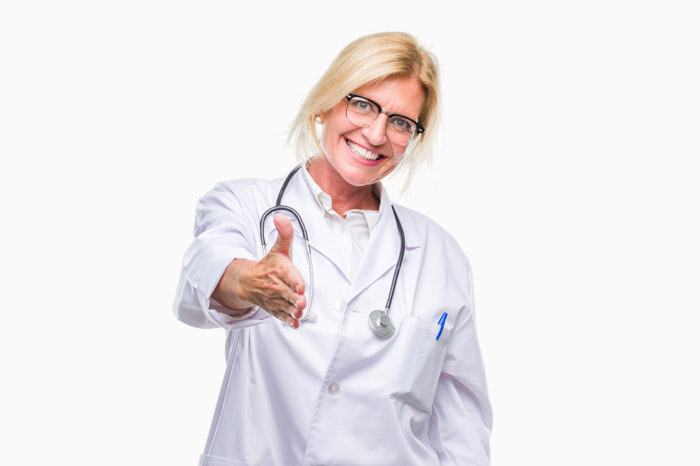 Ärztin mit langen blonden Haaren, Brille und Stethoskop streckt lächelnd ihre rechte Hand aus zur Begrüßung mit einem "Herzlichen Willkommen".